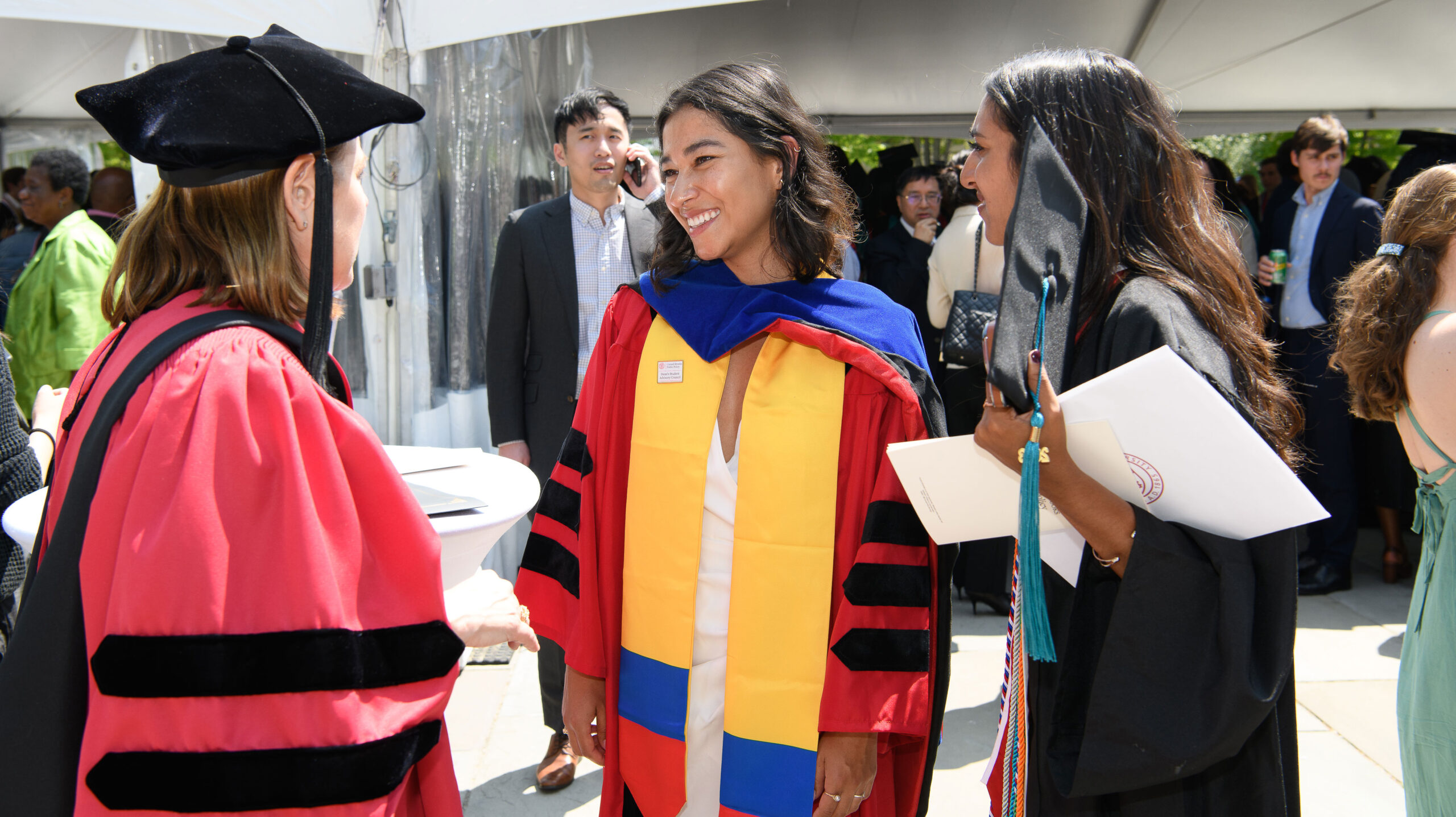 Three women in academic gowns, smiling and talking to each other. 